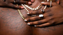 Close-up of hands wearing gold chain, pearl necklace, and diamond ring on tattooed skin.